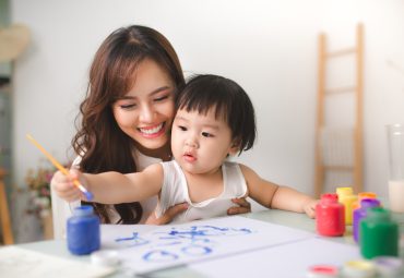 Happy family mother and daughter together paint. Asian woman helps her child girl.